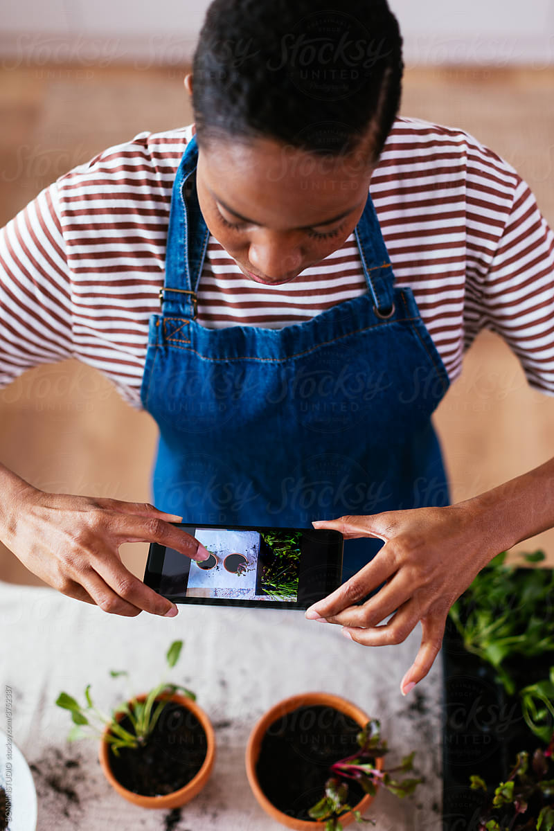 Black gardener taking pictures of potted sprouts