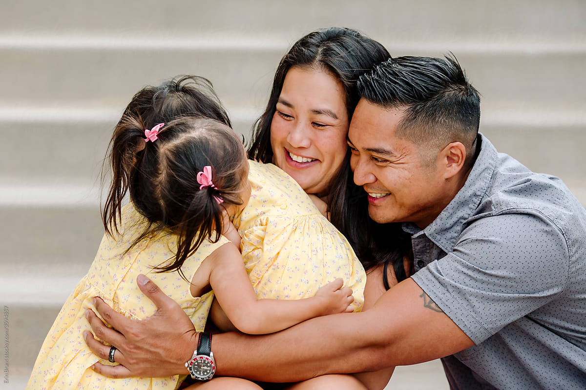 Smiling asian parents with young hugging daughters on steps