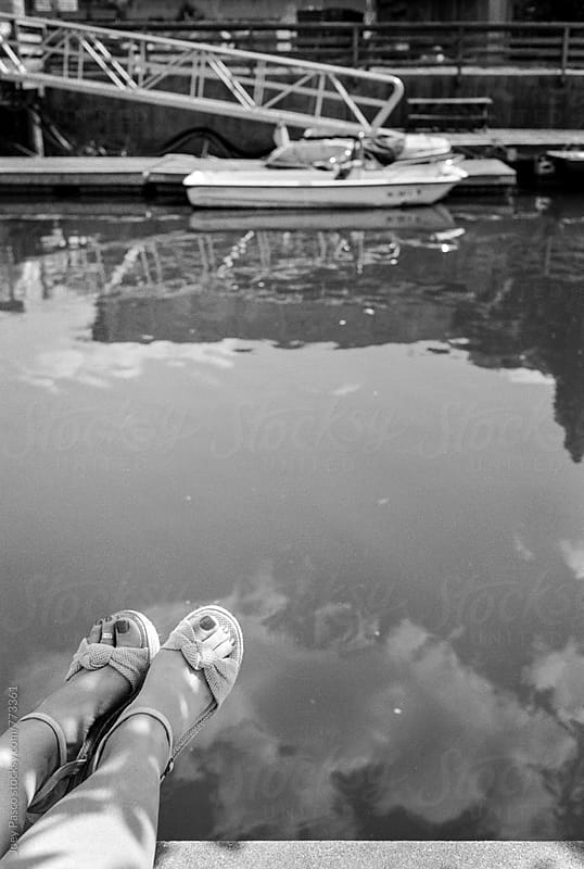 A woman\'s feet dangle over harbor water on a summer day