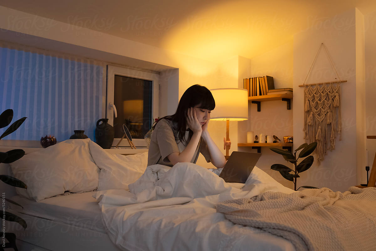 Exhausted Asian woman using laptop in bed