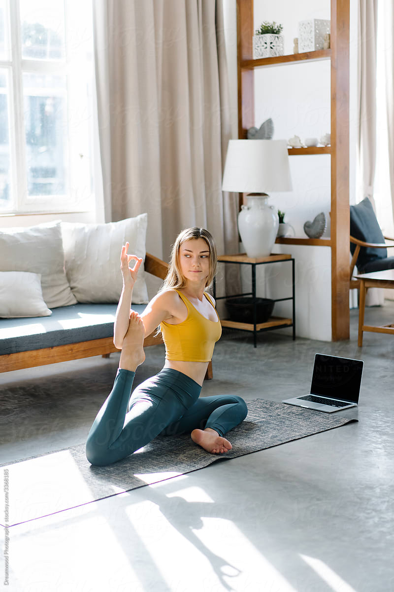 Young woman doing One Legged King Pigeon pose near laptop