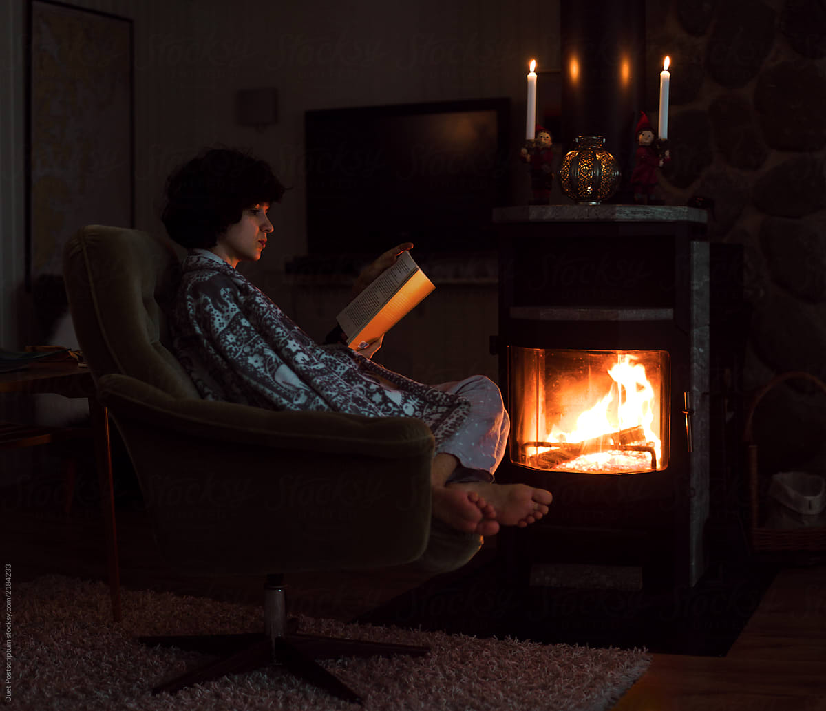 Pretty young woman is reading book near the fireplace.