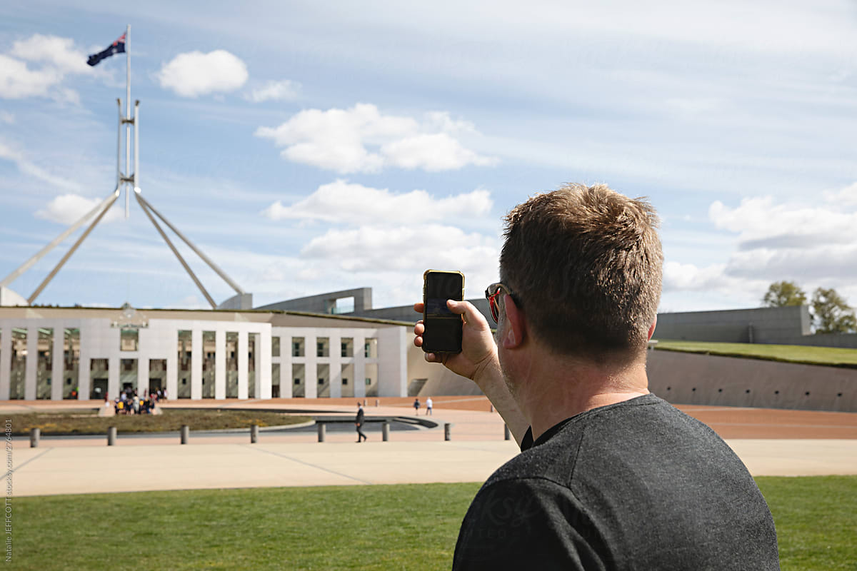 Back of man taking a photo with his phone of Parliament House in Canberra, Australia