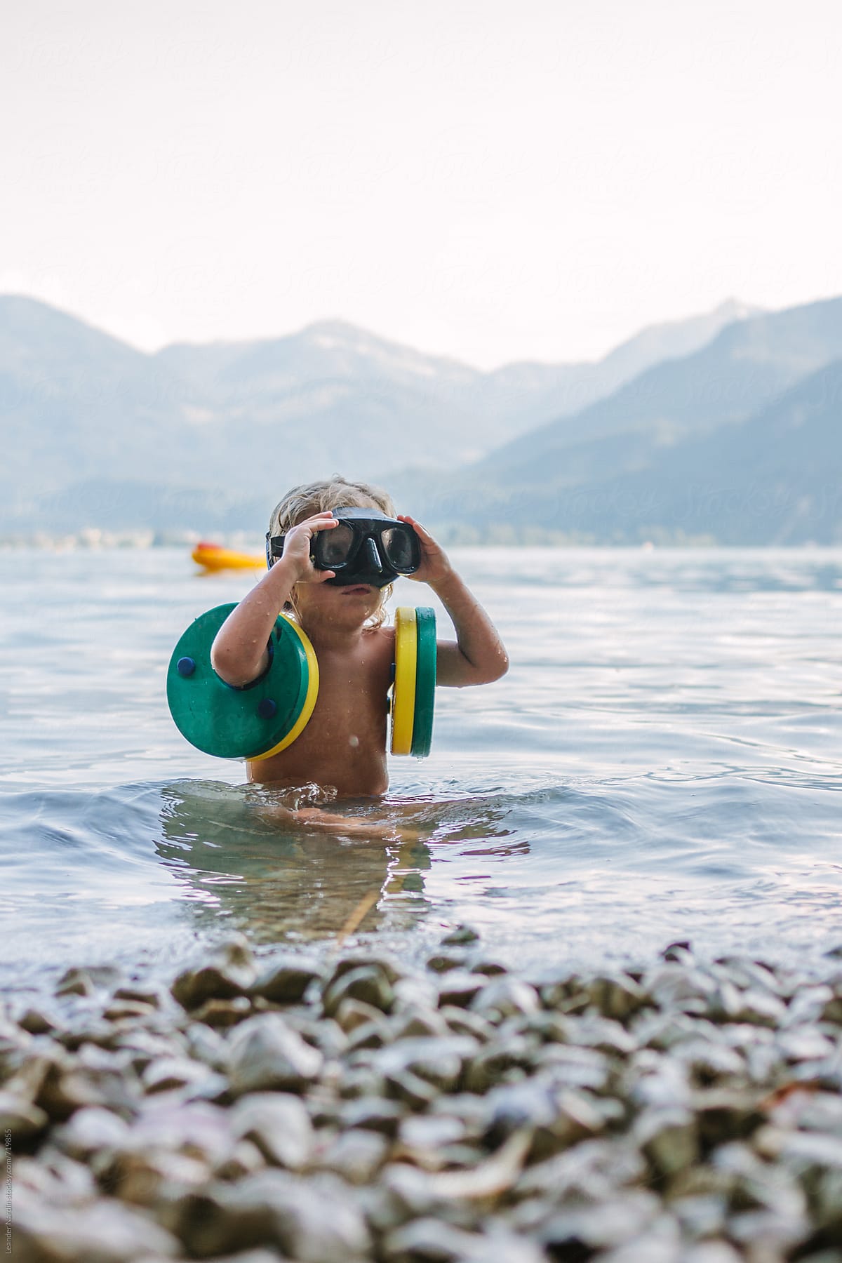 cute little boy with diving goggles and swimming rings playing in the water in a lake