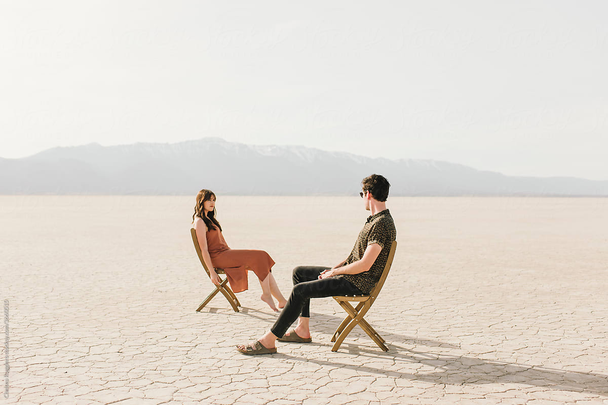 Man and woman sitting in wood chairs in a sunny empty desert