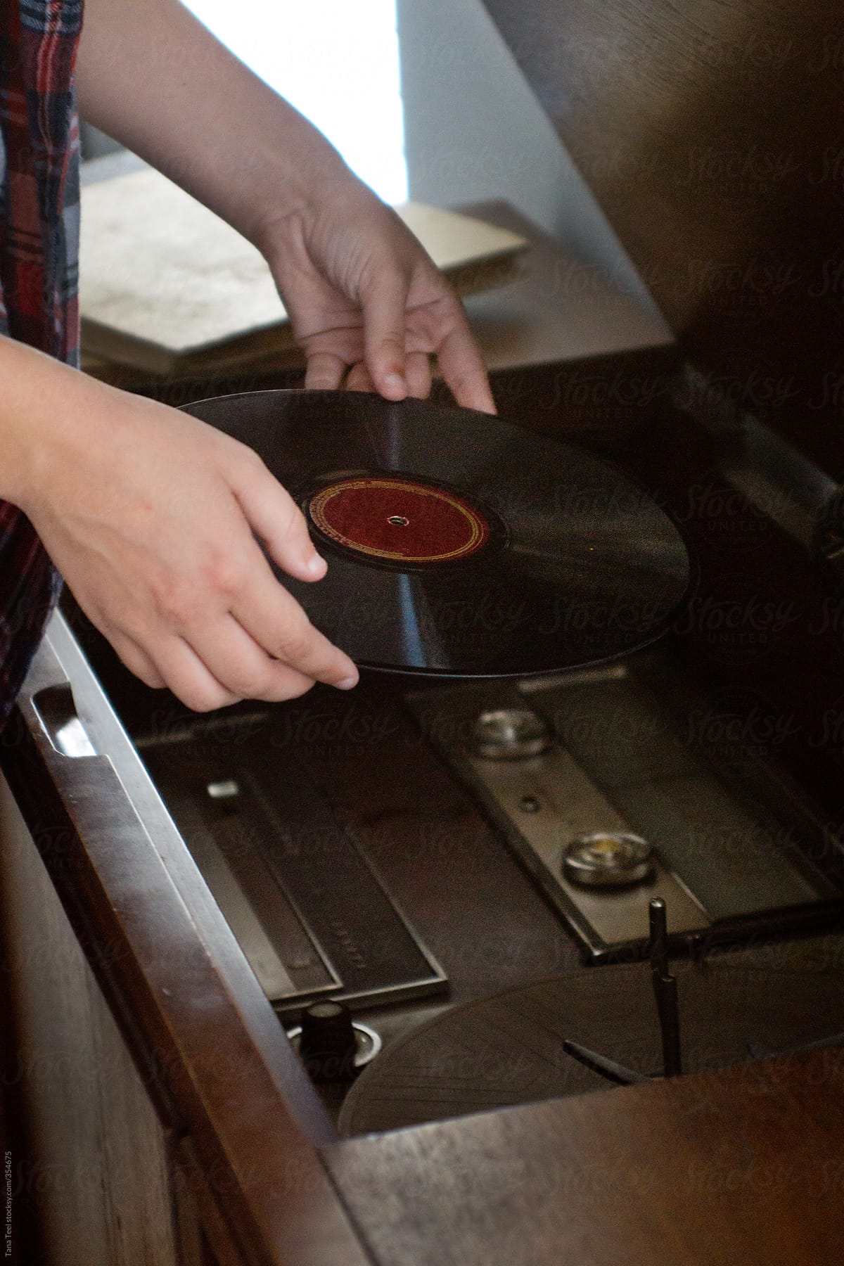 Teen places vinyl 78 record onto turntable in old record player cabinet