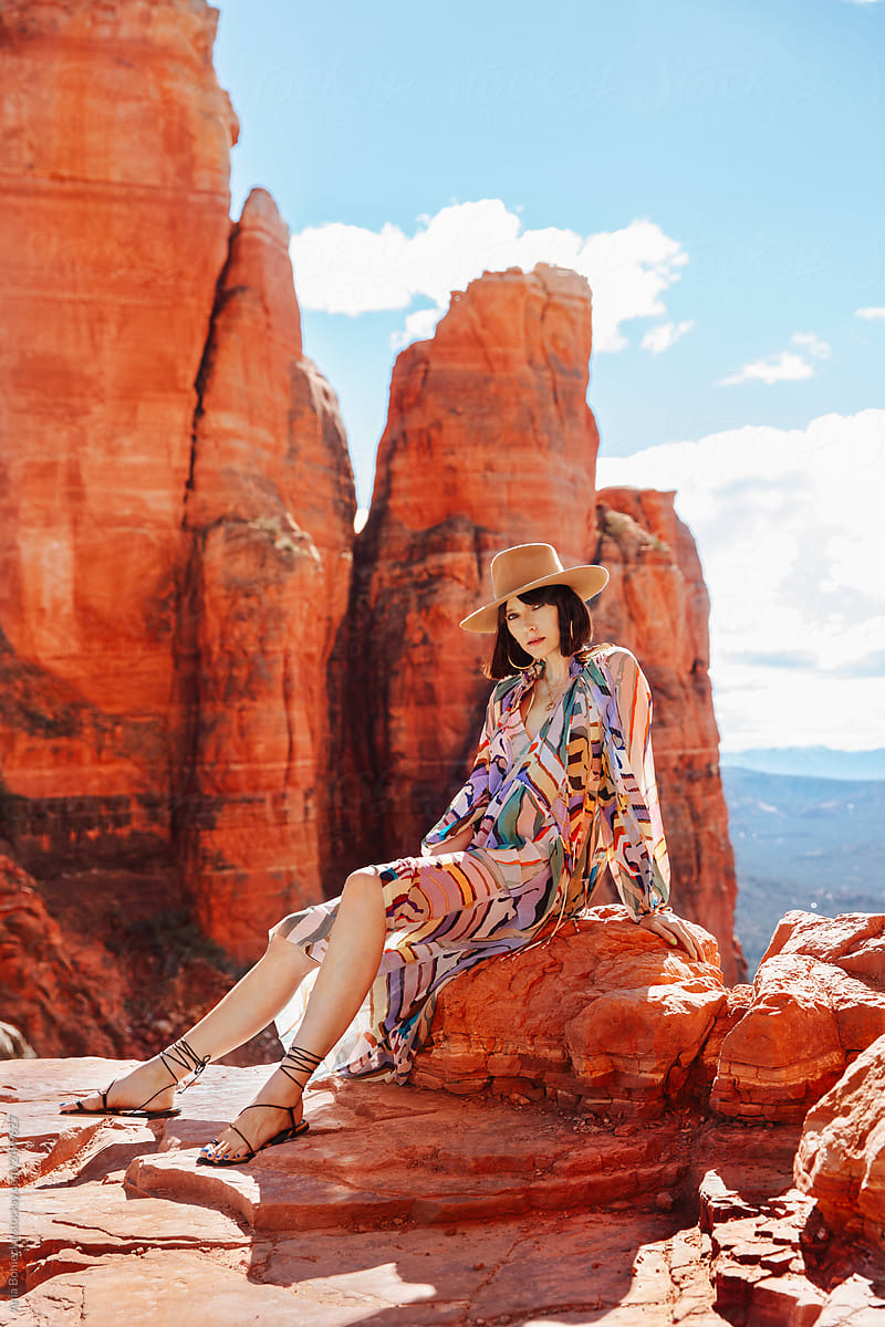 Stylish Cowgirl in dress sits on desert cliff.