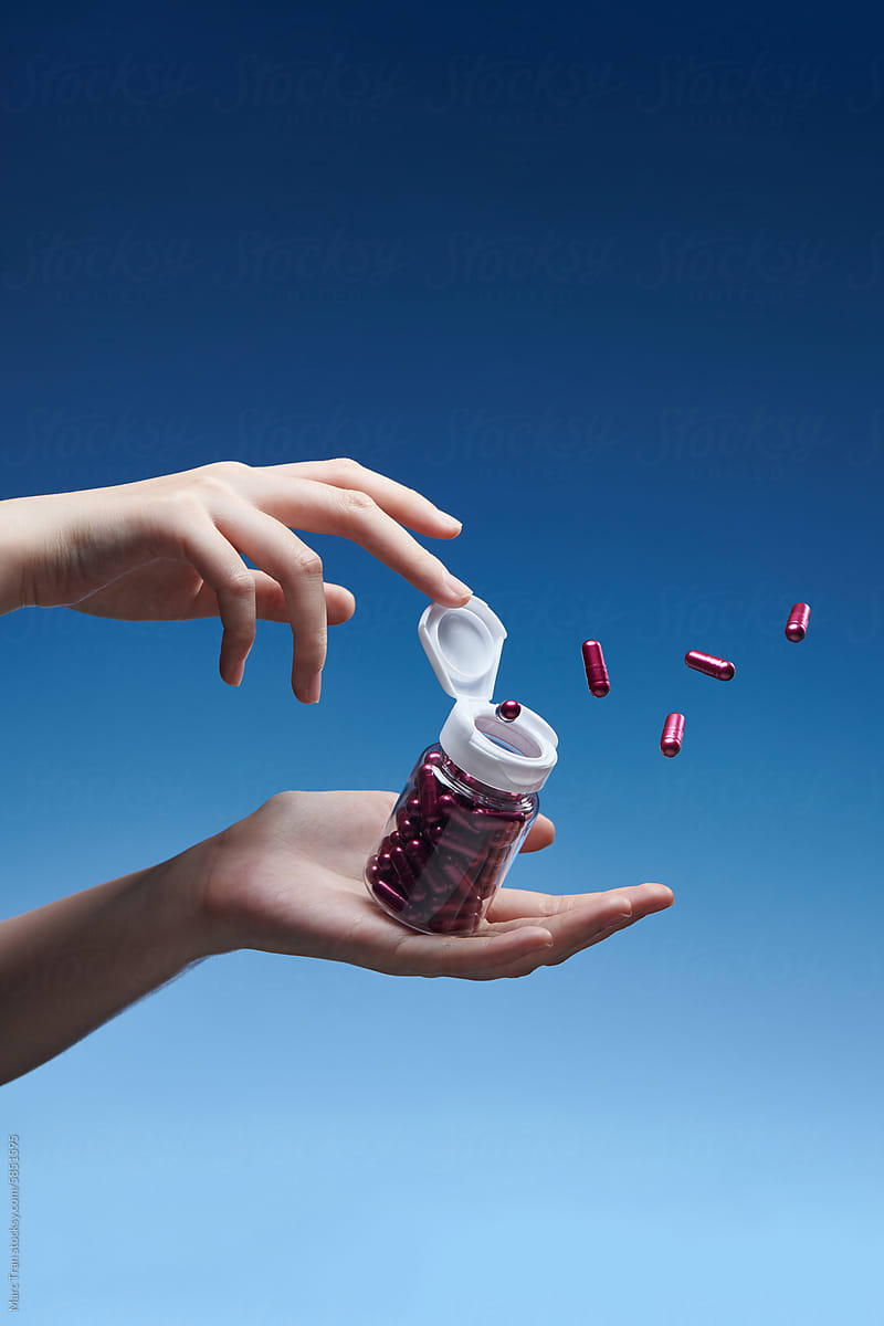 Medicine pills in glass bottle in hand. Isolated on blue white