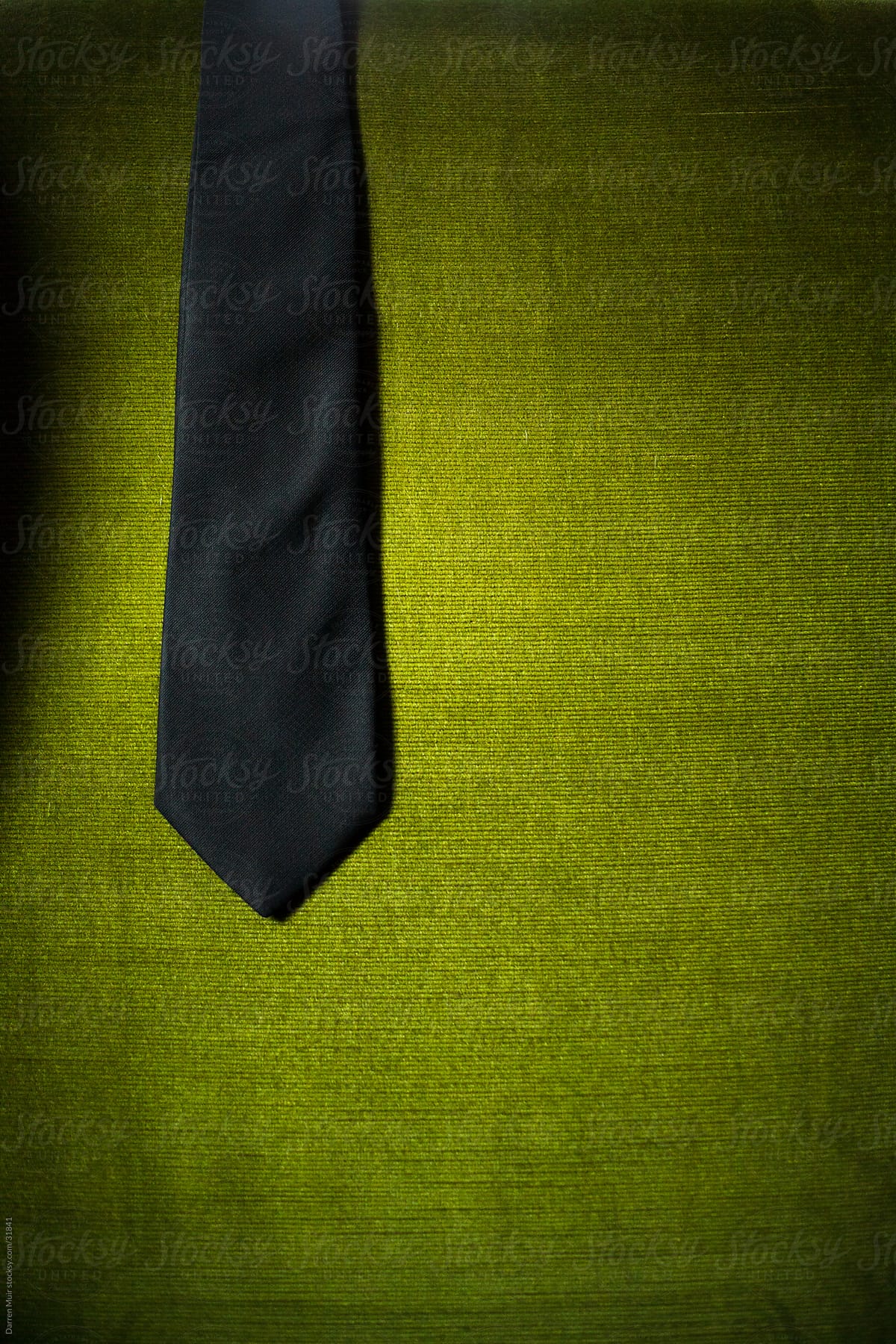 Black tie draped over a green velvet chair.