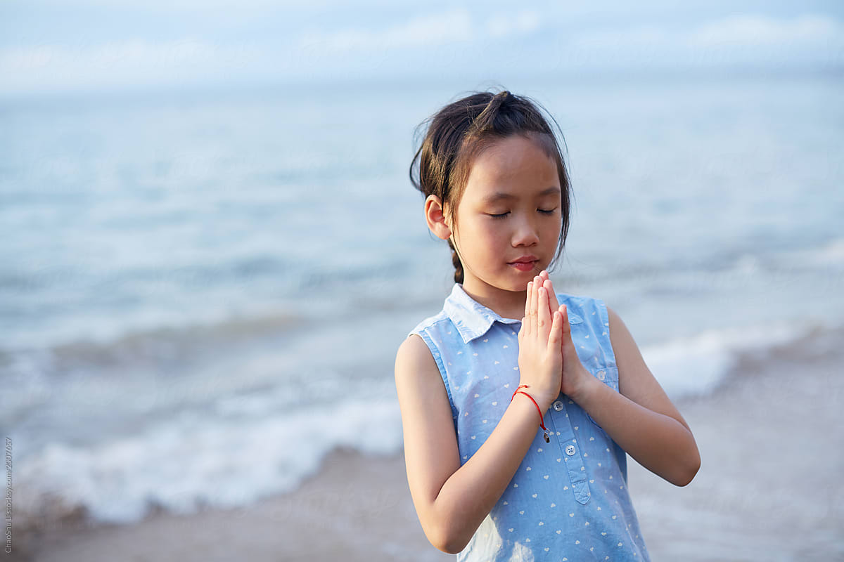 Cute beautiful asian little girl praying with hands closed at the seaside