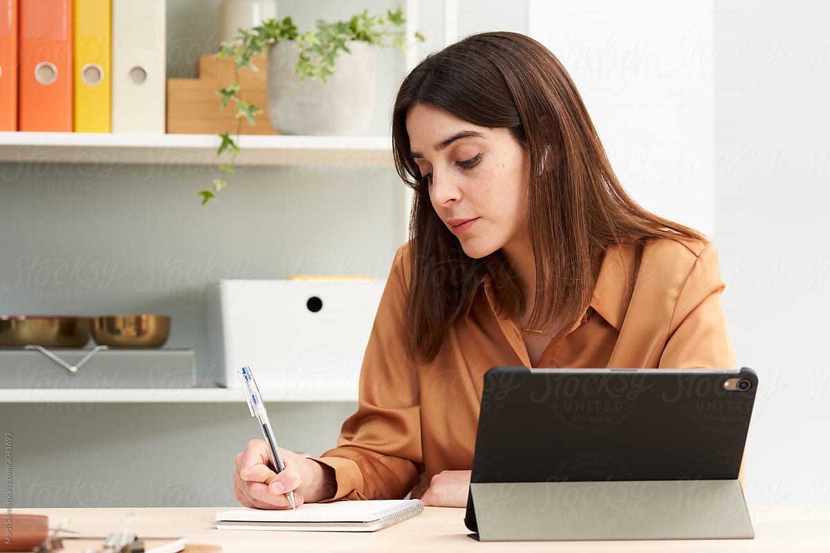 Smart woman writing in notebook in home office