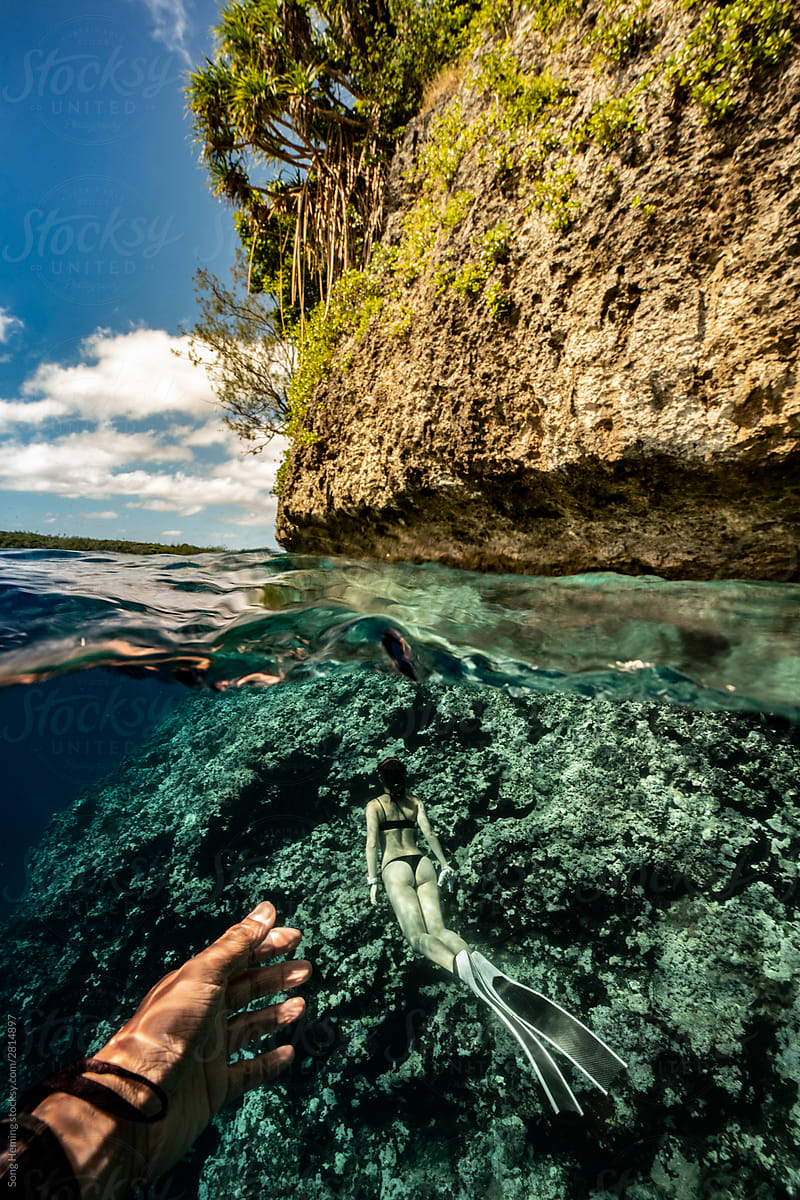 Photographer stretch out hand to female diving half underwater