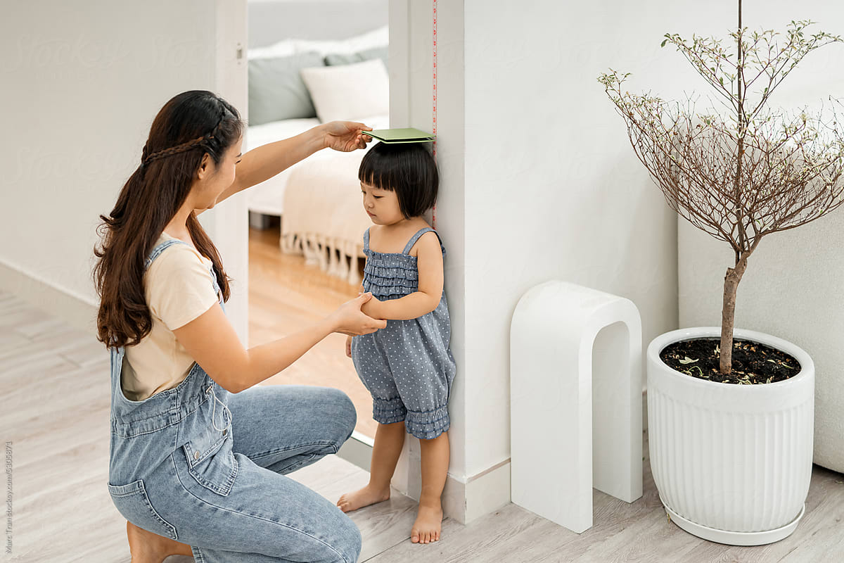 Woman measuring height of her little daughter at home