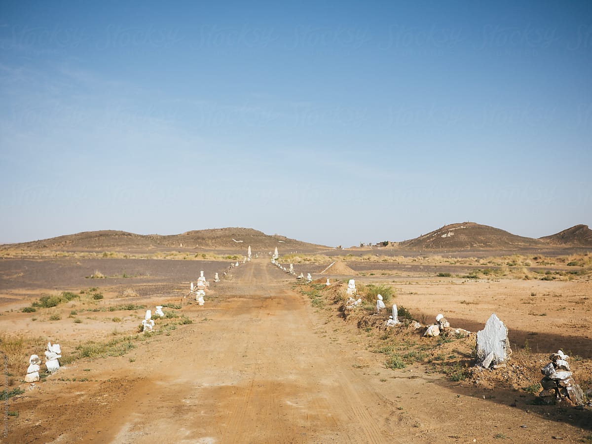 Road in the desert with stones by sides leading to the hills