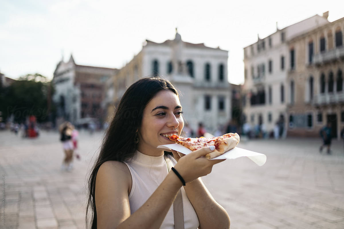 Young woman eating a slice of pizza on the street in Italy