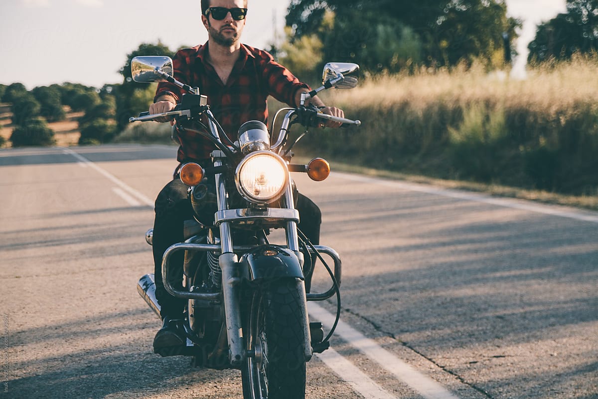 Man in shirt with sunglasses driving his motorbike on a road at sunset