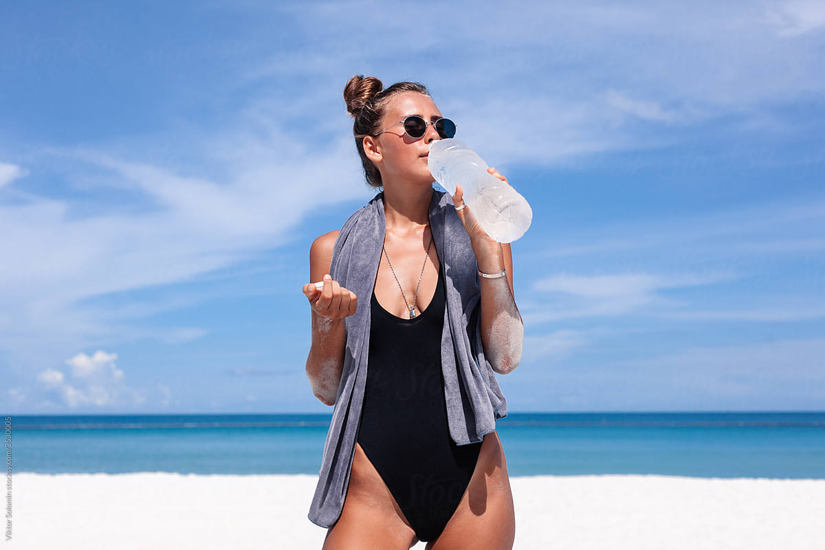 Woman in swimsuit drinking water on beach