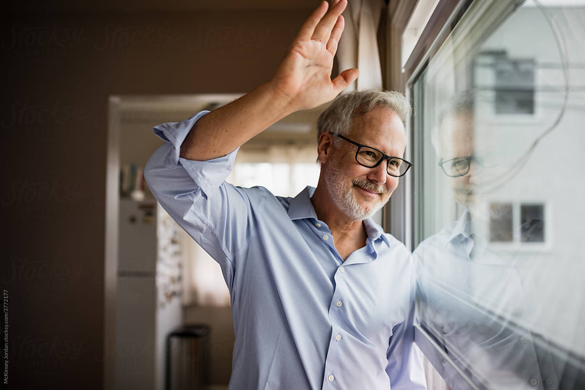 Friendly Man Gives a Neighborly Wave While Looking Out His Apartment Window