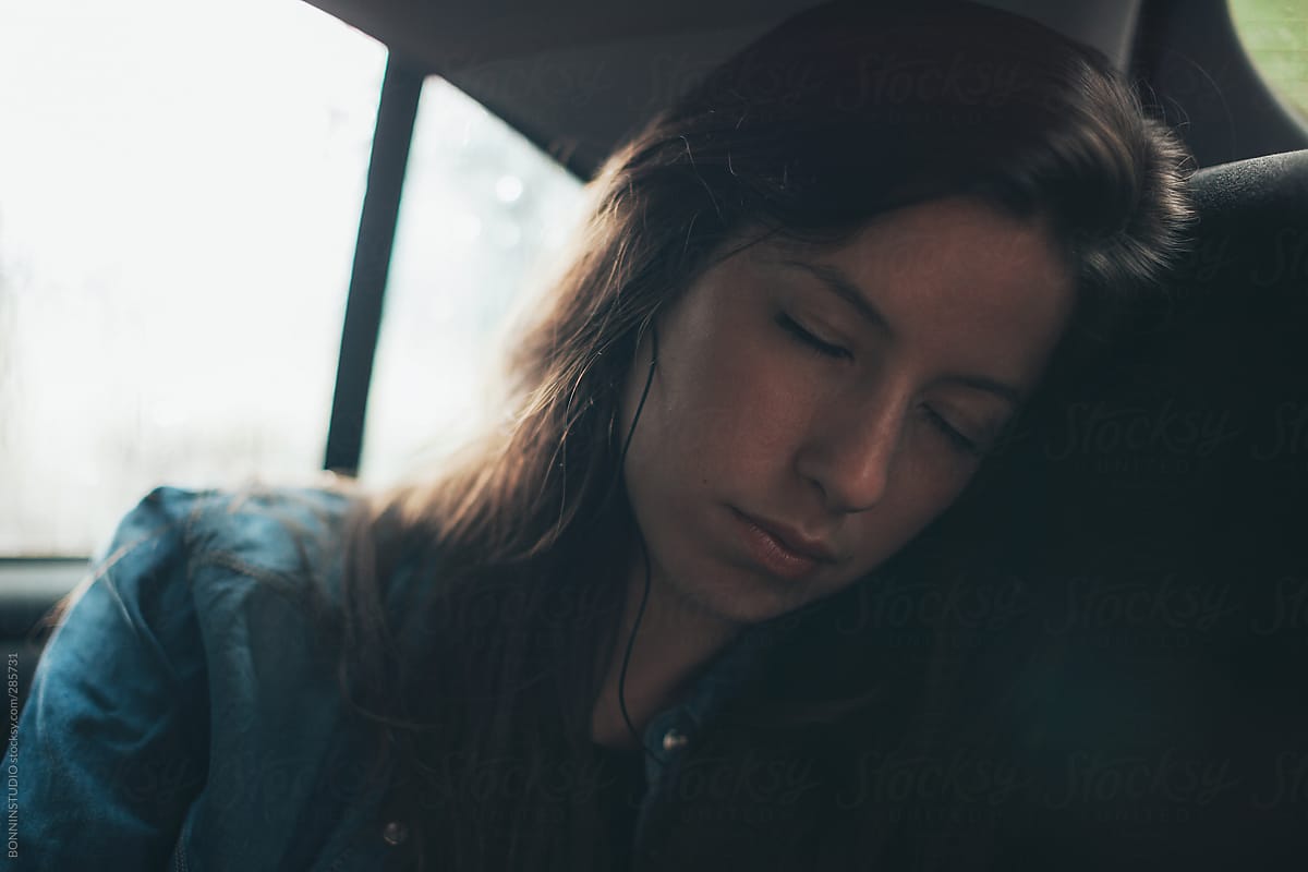 Tired young woman sleeping and listening music  inside a car. Road trip.