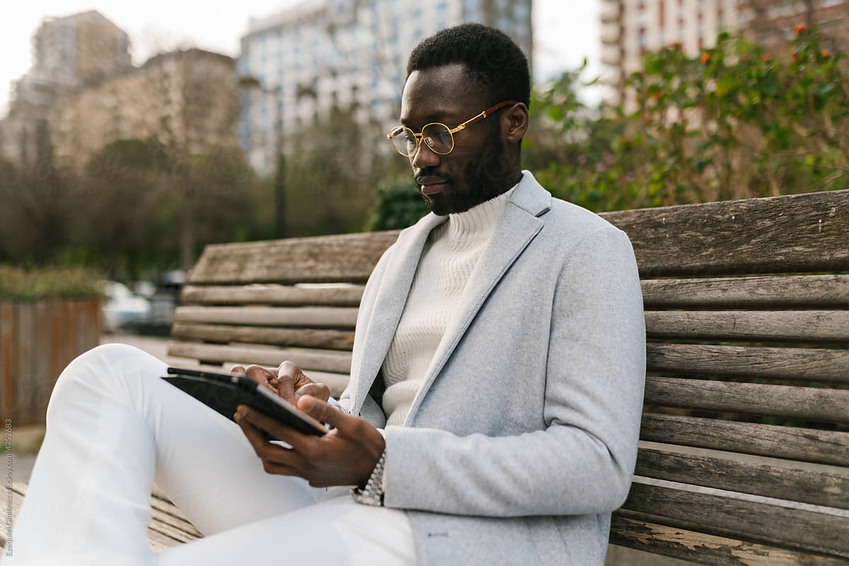 Elegant black man using tablet on bench in park