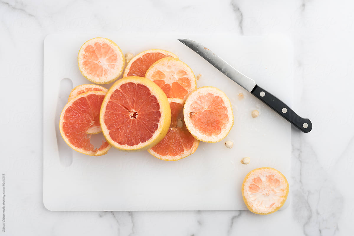 Cut up messy grapefruit slices on a cutting board and marble tabletop