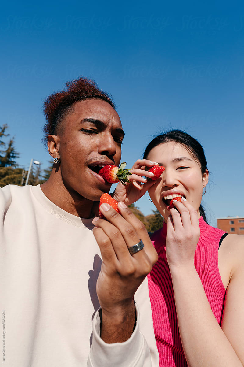 Funny selfie of multiracial couple eating strawberries