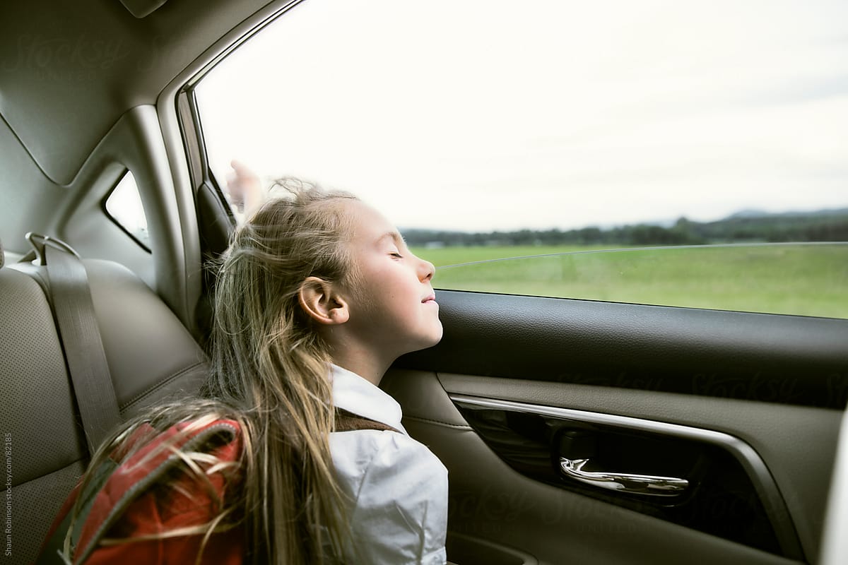 a school girl in the back of the car with her hair blowing in the wind