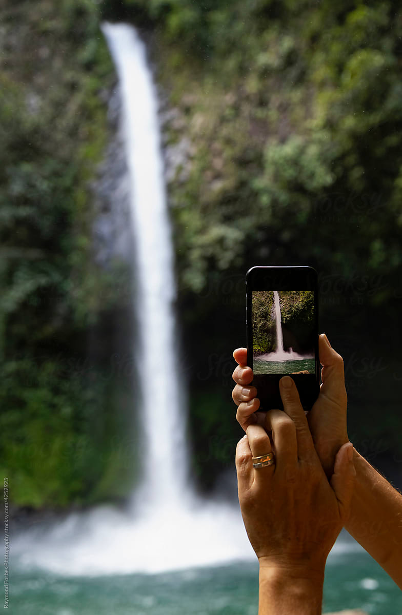 Woman pressing button taking picture of waterfall