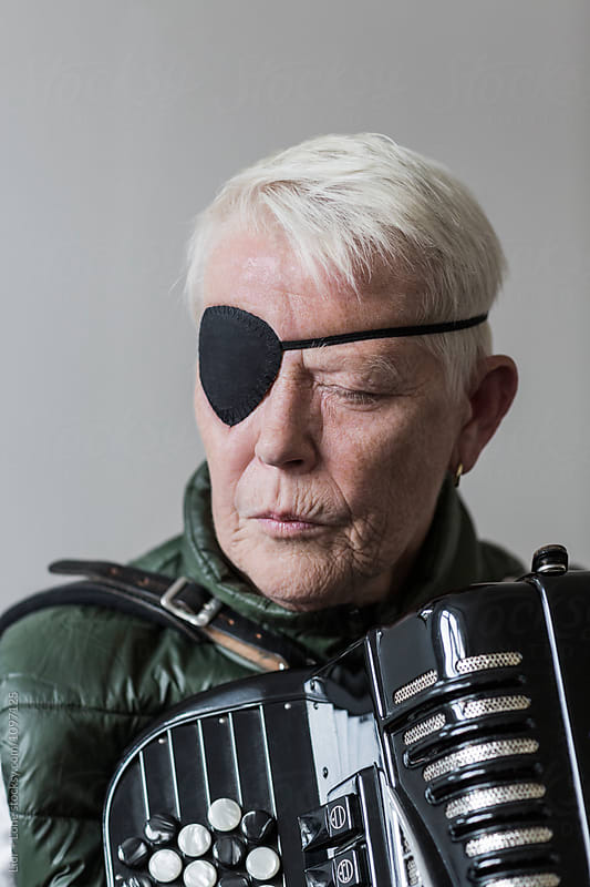 Senior woman with eye patch holding an accordion eyes shut