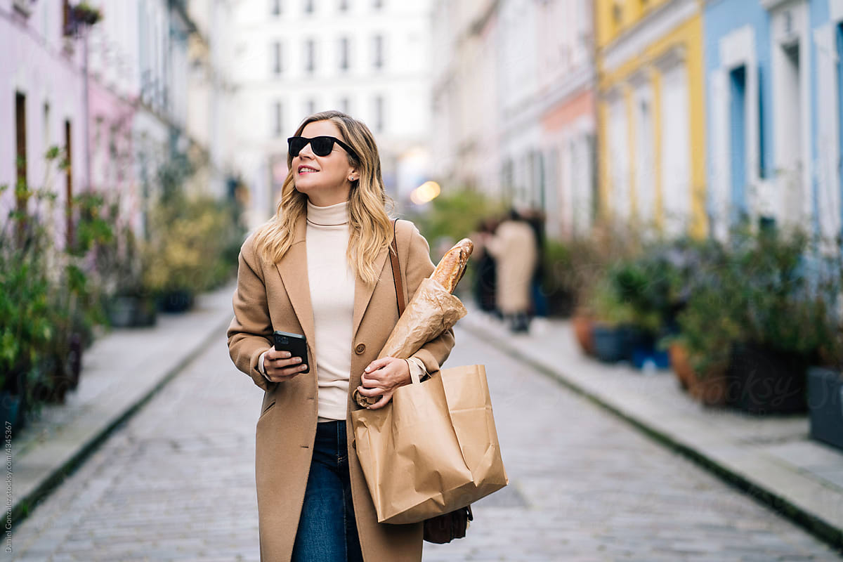Woman with baguette and cellphone walking on street