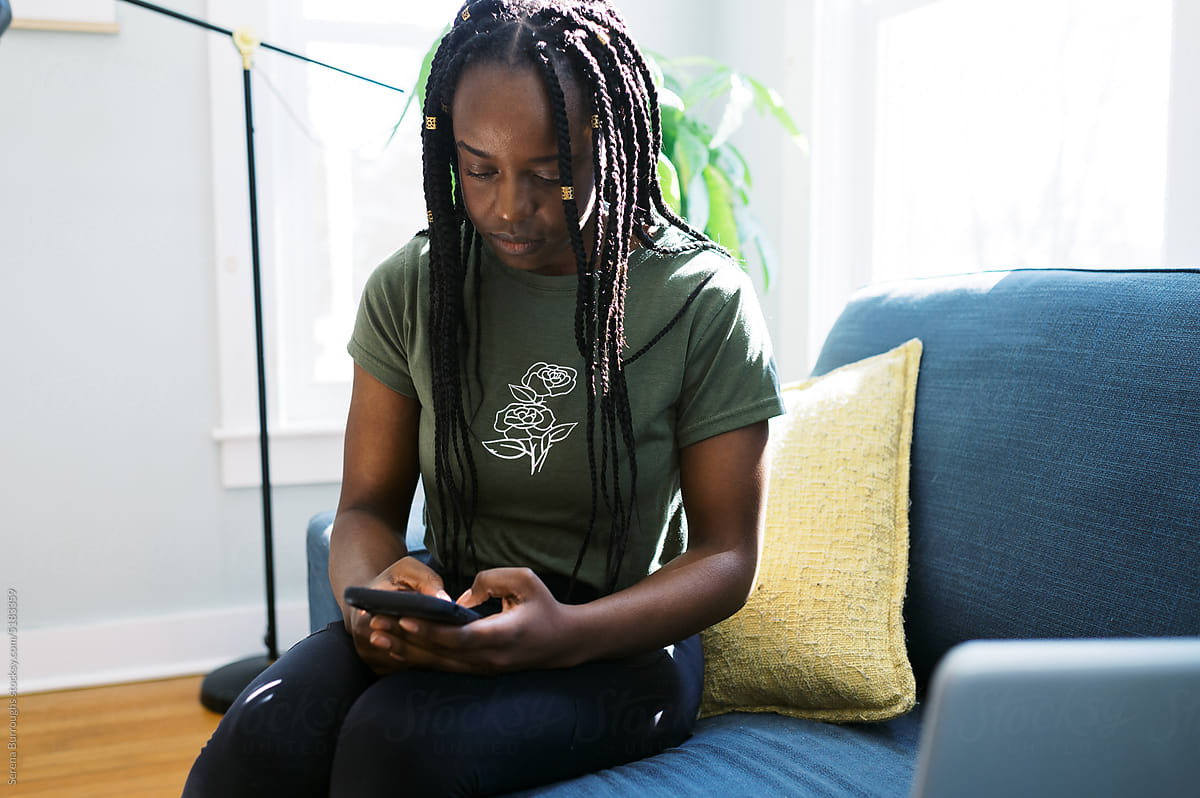 smiling black woman sitting in living room while using her phone