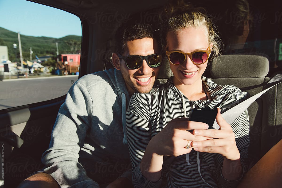 Guy and girl using smart phone in the backseat of a car.