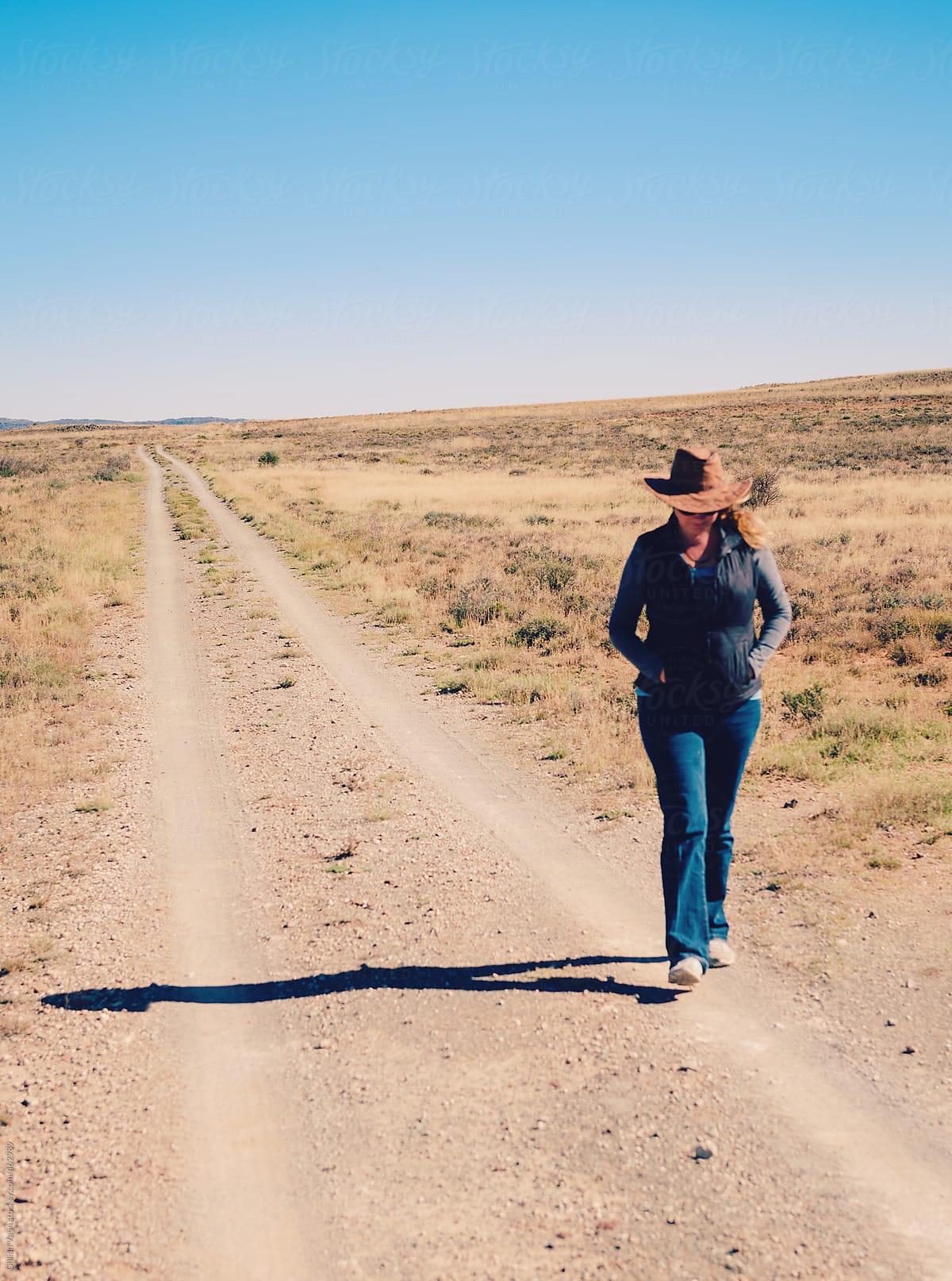 woman walking on dirt road in a flat, dry, rural scene