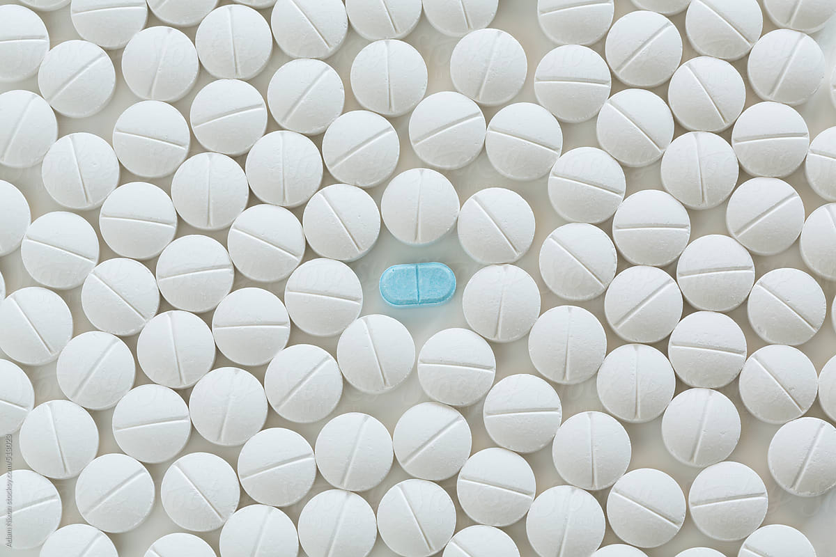 One blue pill surrounded by white prescription pills on white background