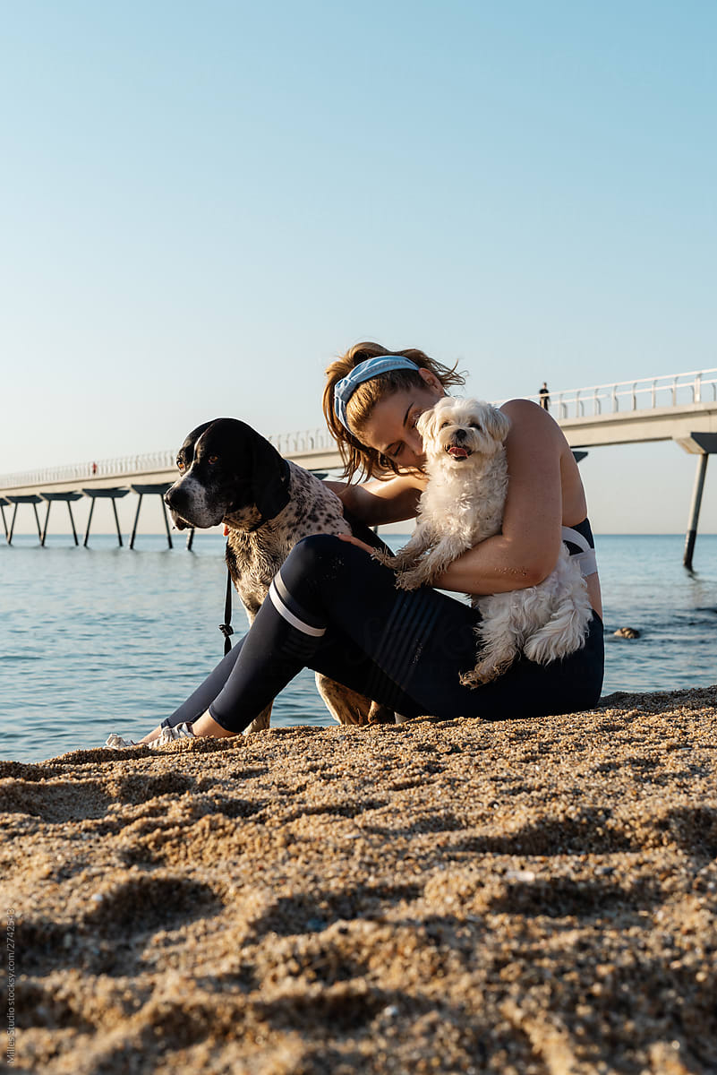Female owner hugging and kissing dogs on beach