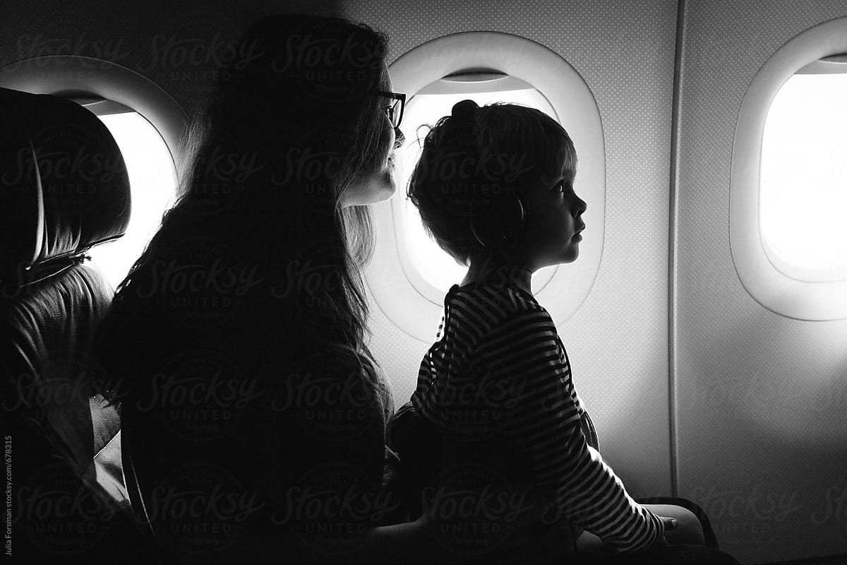 Child sitting on mom\'s lap with earphones on, while on an aeroplane.