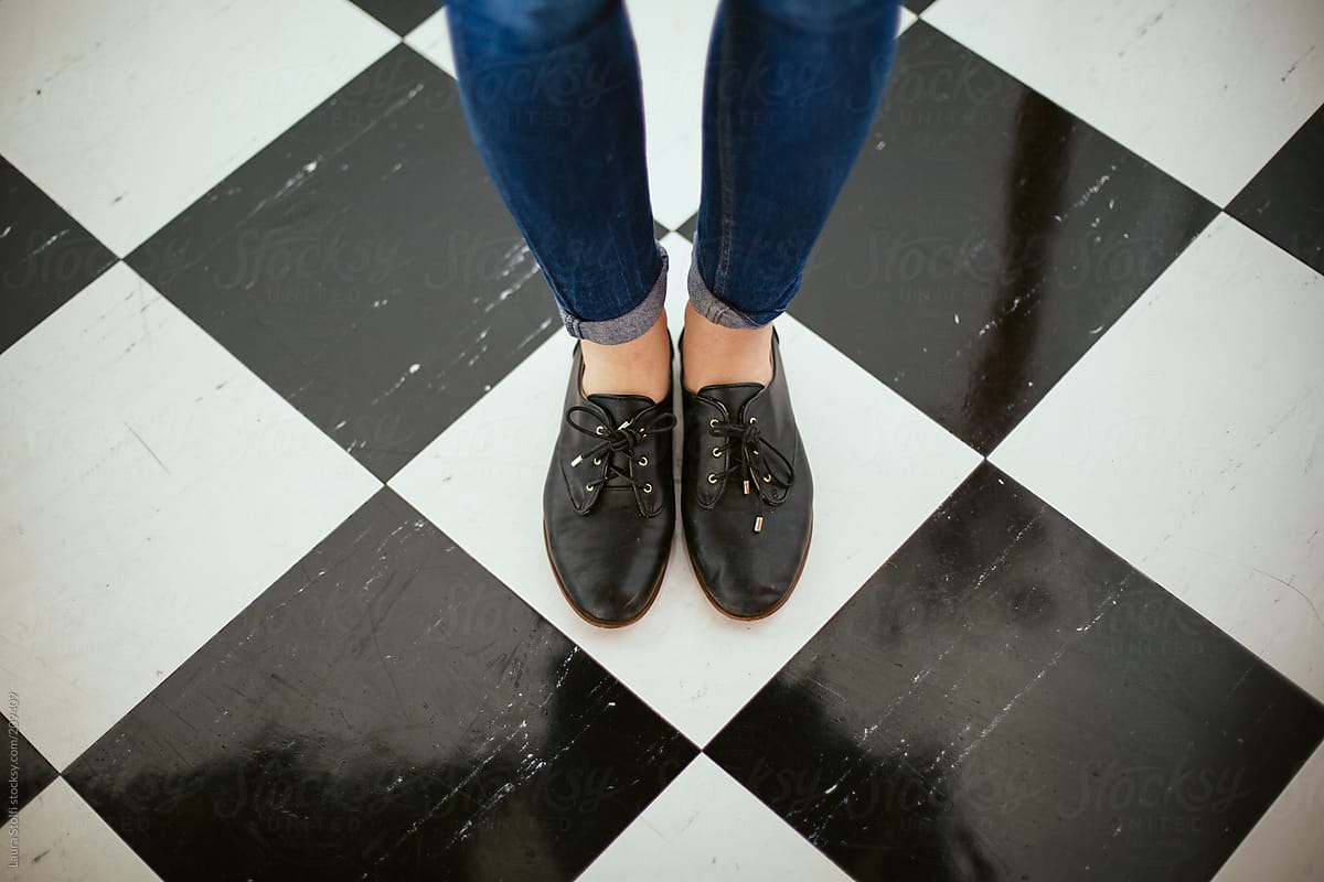 Girl wearing black leather lace-ups and jeans stands on checked flooring