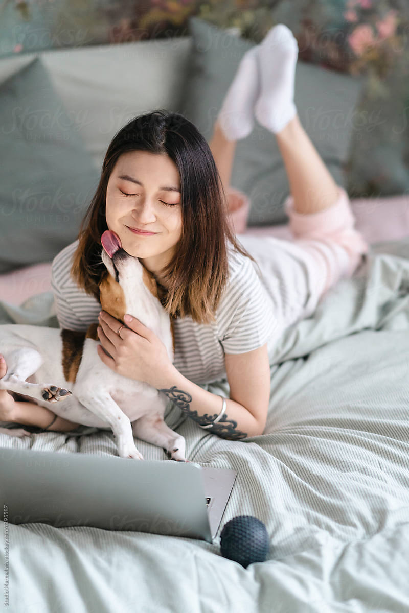 Happy woman lying with dog on bed
