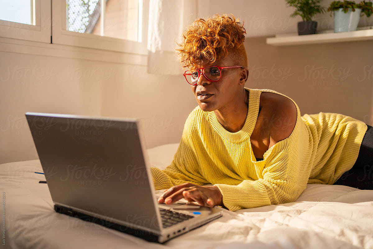 Modern Woman With Glasses Using Her Laptop Laying On The Bed.