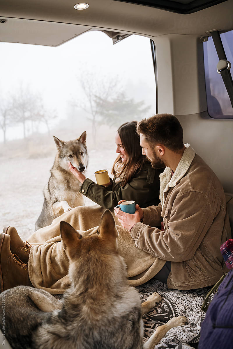 Young couple in a camper van in nature during winter with cute dog having warm coffe