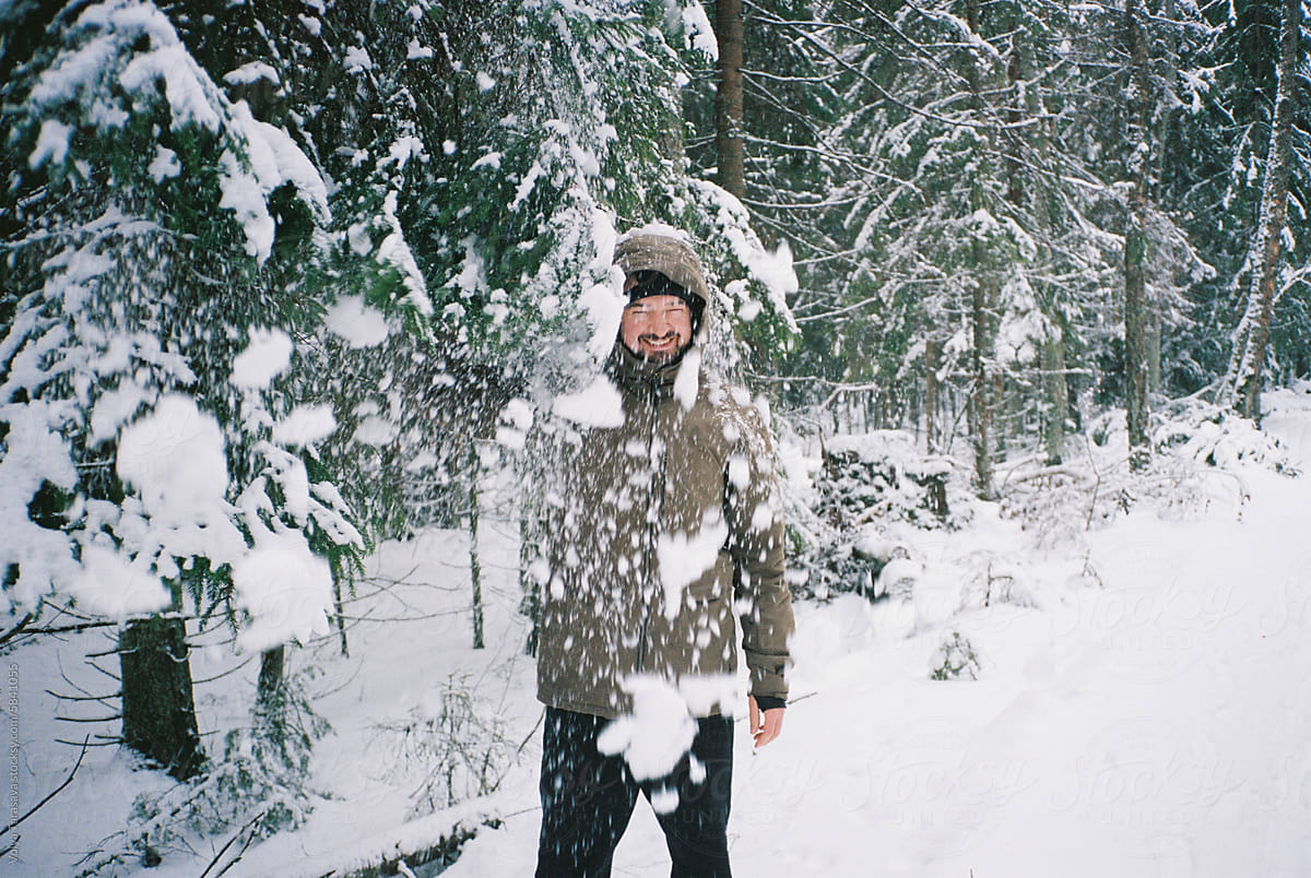 Young laughing man under the falling snow in winter forest