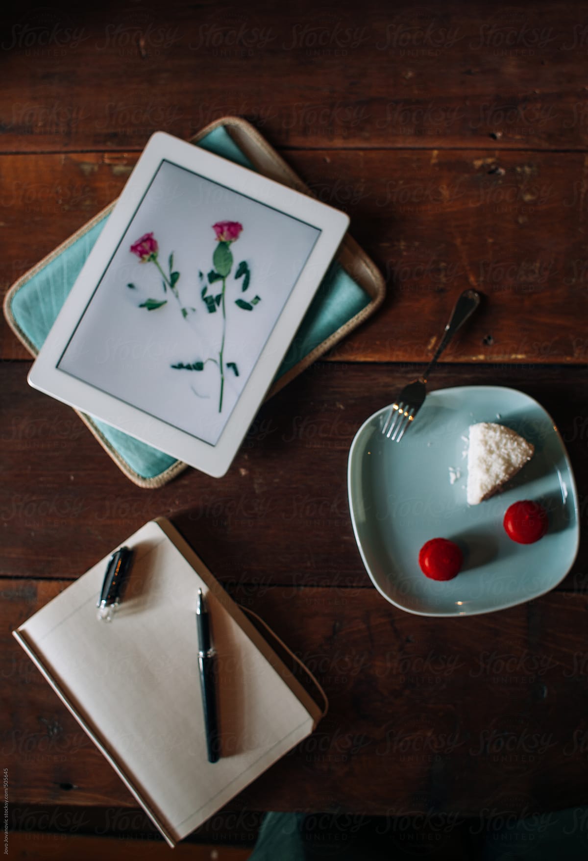 Tablet showing flowers, cake and notebook on table