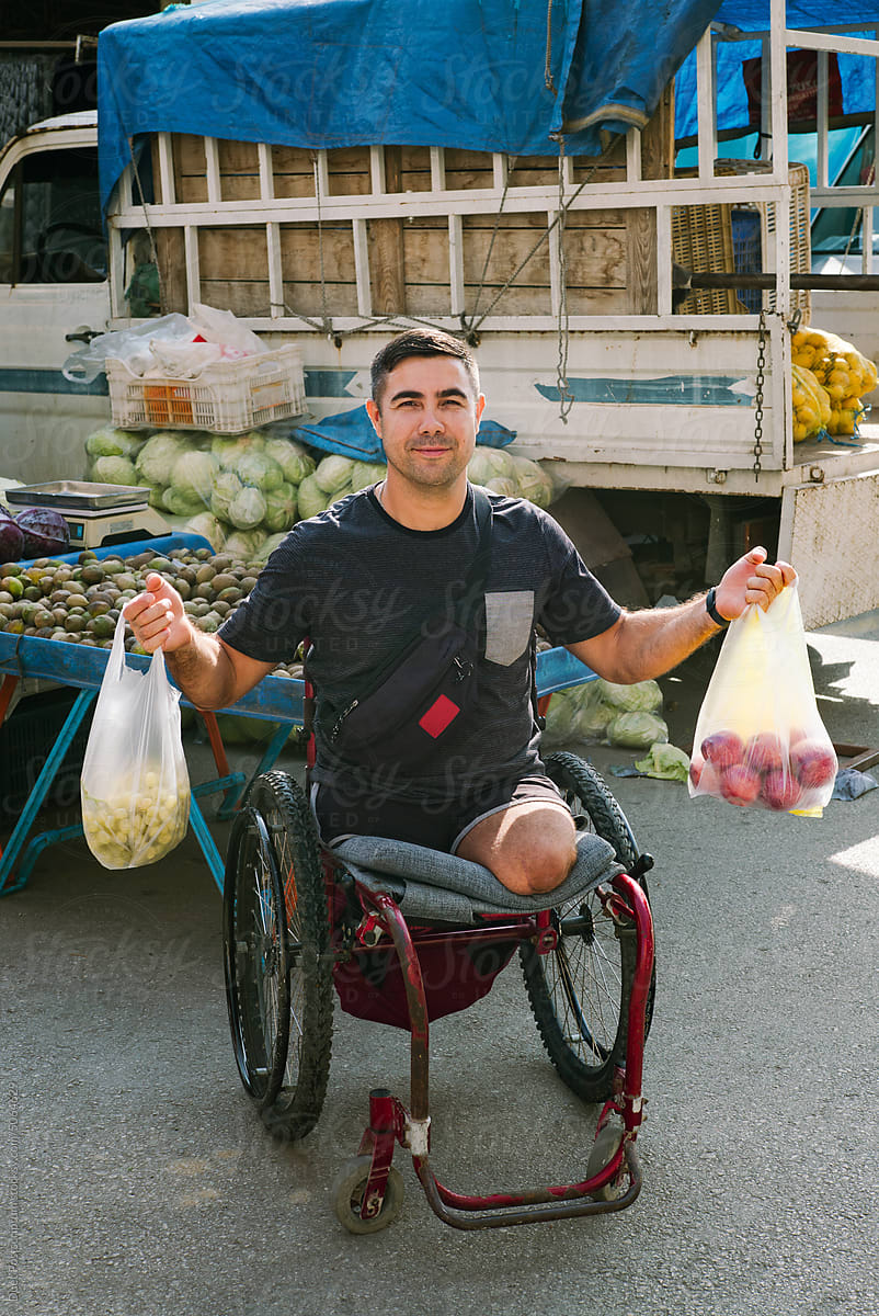 Adult man in a wheelchair with groceries in plastic bags.