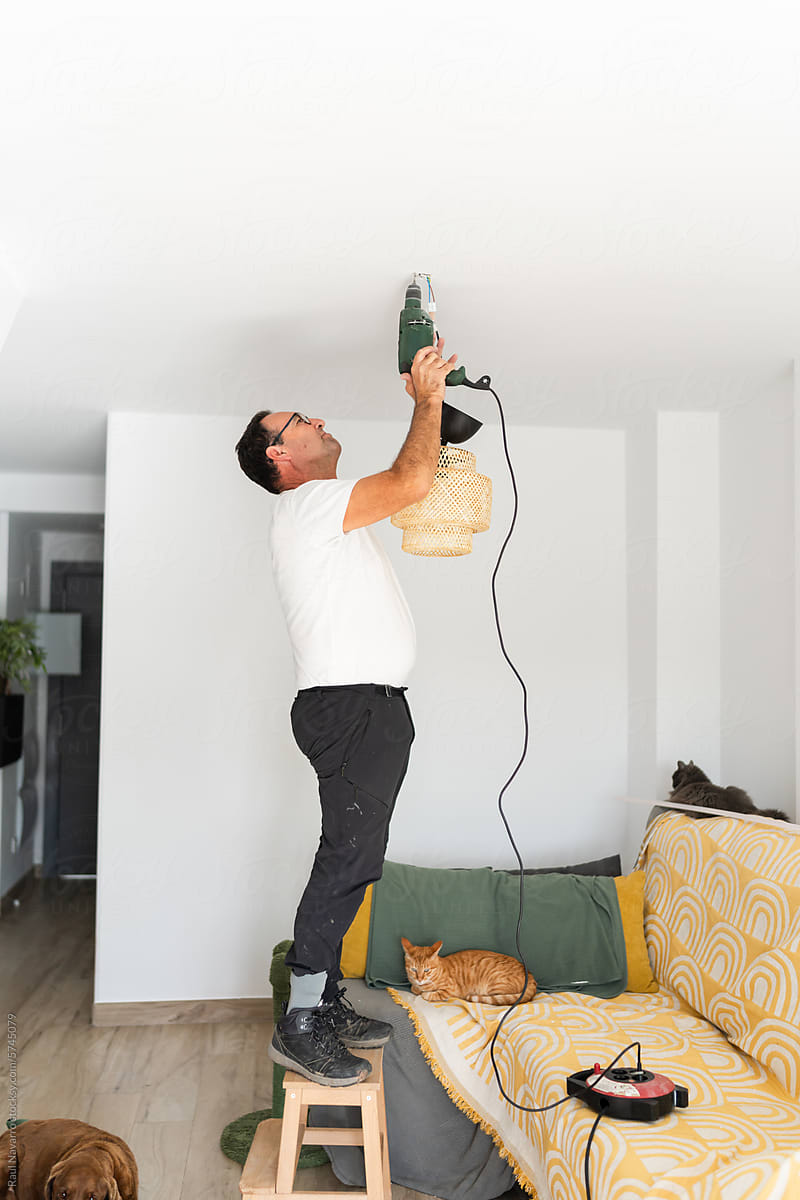 senior man using a drill to place a lamp on the ceiling.