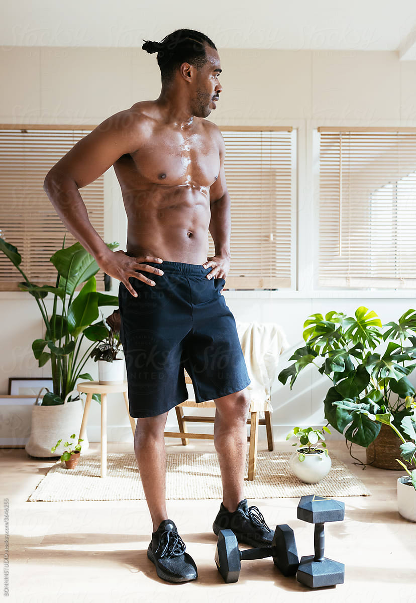 Shirtless ethnic athlete resting near dumbbells at home