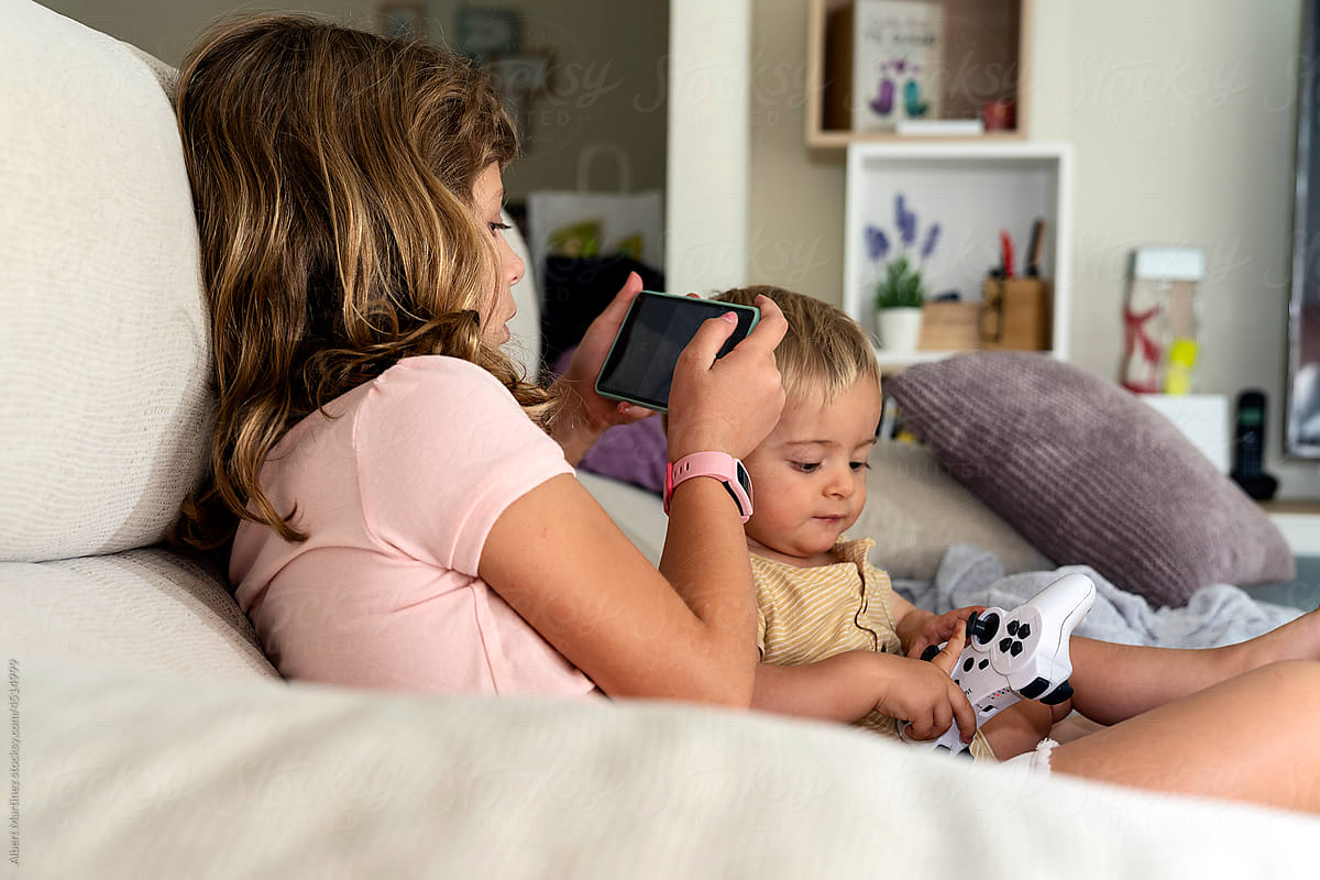 Girl watching video on smartphone near curious baby