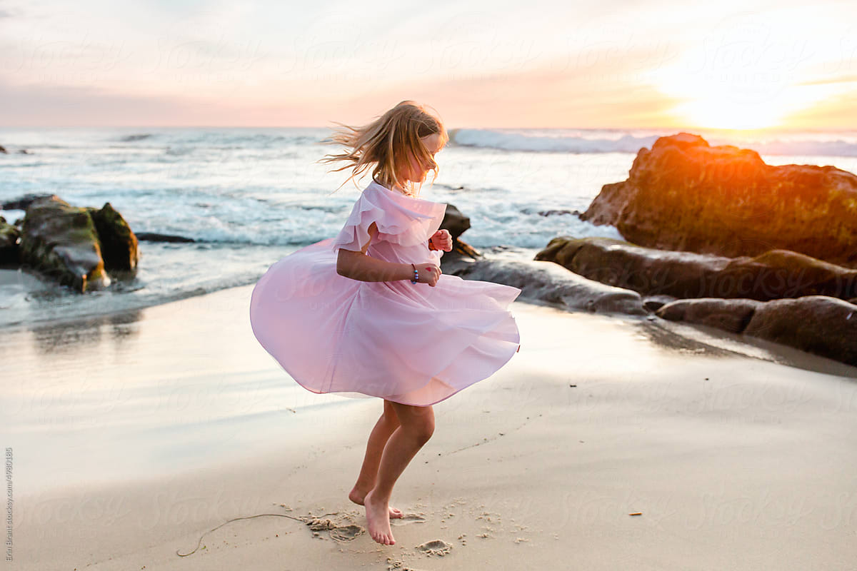 Happy tween girl in pink dress dancing on beach