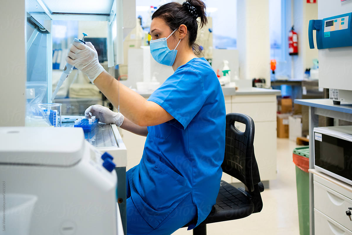 Woman With Mask And Blue Uniform Working In The Lab.