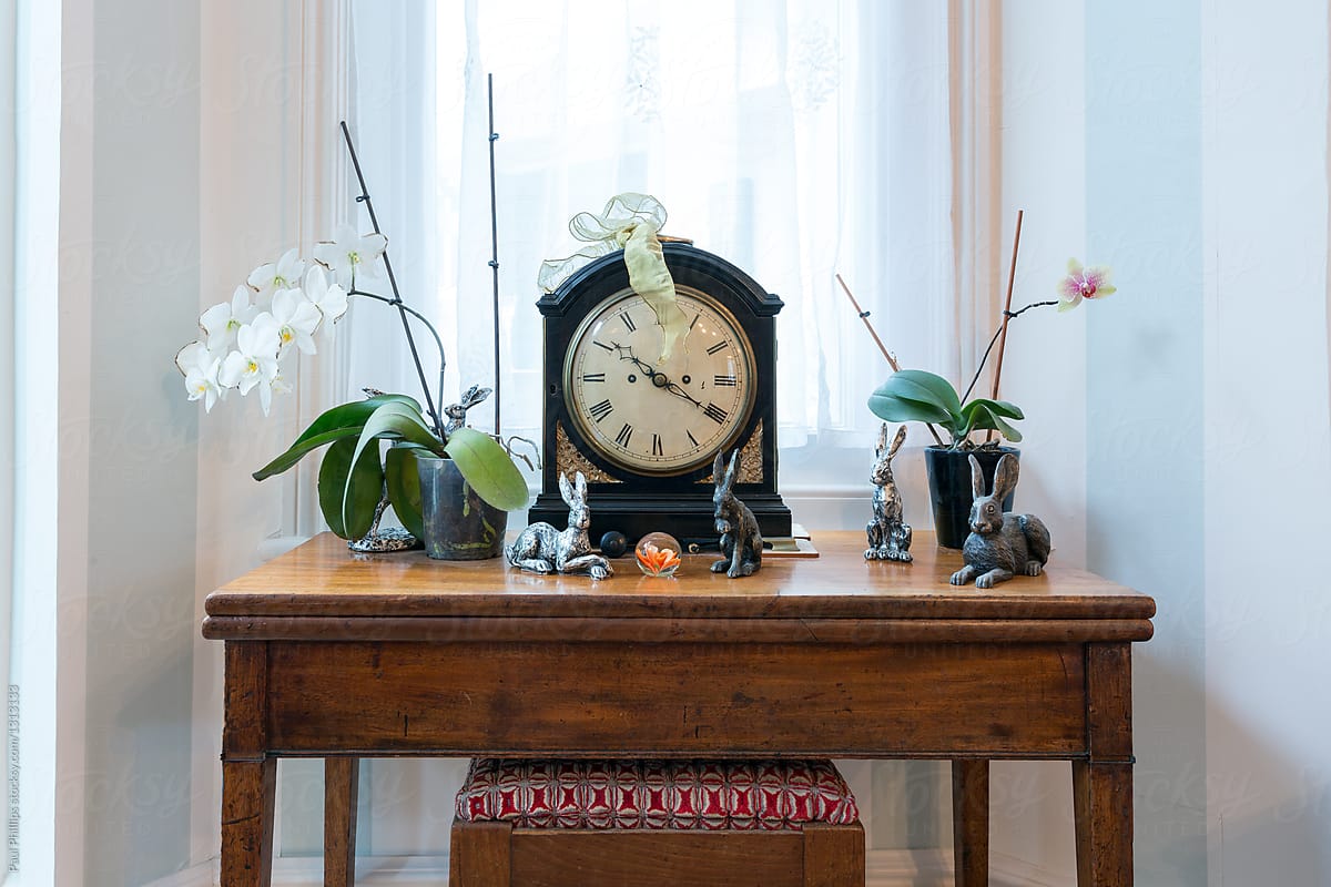 Antique clock on an old table with flowers by a window.