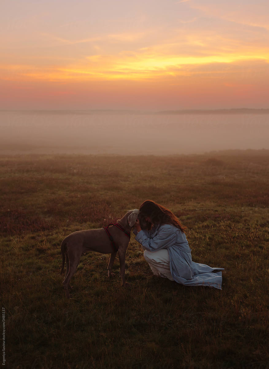 A girl in a blue coat with a dog in the foggy field